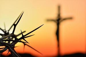 doornenkroon van Jezus Christus tegen silhouet van katholiek kruis bij zonsondergang op de achtergrond