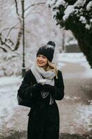 jong vrouw in warm kleren genieten van in sneeuw met meenemen koffie kop foto