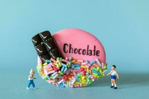 miniatuur kinderen met chocola koekje staand tegen een blauw achtergrond. wereld chocola dag concept foto