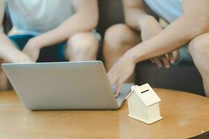 Aziatisch homo paar buying nieuw droom huis of eigendom met laptop en huis model- Aan tafel. concept voor huwelijk, lening, financiën, verzekering, hypotheek, echt landgoed en eigendom. foto