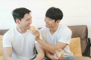 gelukkig Aziatisch homo paar aan het eten koekje en genieten grappig moment. concept lgbt homo. lgbt paren voeden koekjes. foto