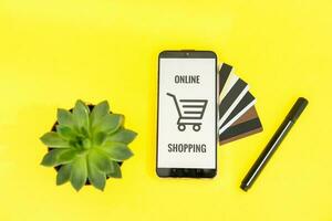 smartphone met de inschrijving-online boodschappen doen detailopname. online winkelen, online bankieren, online betaling. betaling met plastic kaarten. vlak ley Aan een geel achtergrond. foto