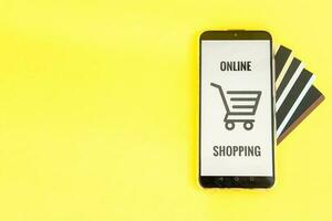 smartphone met de inschrijving-online boodschappen doen detailopname. online winkelen, online bankieren, online betaling. betaling met plastic kaarten. vlak ley Aan een geel achtergrond. foto