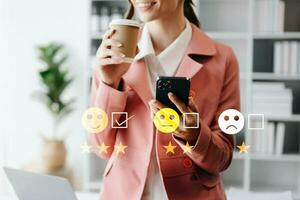 klant onderhoud evaluatie concept. zakenvrouw drukken gezicht glimlach emoticon tonen Aan virtueel scherm Bij tablet en smartphone foto