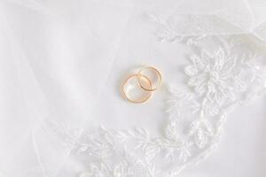 wit bruiloft tule achtergrond met borduurwerk met twee goud bruiloft ringen. top visie. een kopiëren van de ruimte. foto