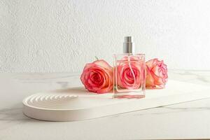 een elegant fles van parfum tegen de achtergrond van vers roze rozen staat Aan een wit podium in de het formulier van een boog. een modern beeld van parfum. foto