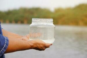 detailopname handen houden transparant pot dat bevatten monster water van de meer. concept, ontdekken, inspecteren kwaliteit van water van natuurlijk bron. ecologie vragenlijst. milieu behoud. foto