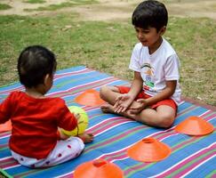 twee gelukkig jongens in maatschappij park, gelukkig Aziatisch broers wie zijn glimlachen gelukkig samen. broers Speel buitenshuis in zomer, het beste vrienden. kleuter baby jongen spelen met zijn gelukkig broer in de tuin foto