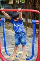 Aziatisch jongen aan het doen routine- oefening in maatschappij park gedurende de ochtend- tijd. schattig weinig kind oefening en Sportschool naar houden zichzelf fit voor leven. kind oefening buitenshuis schieten foto