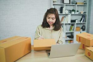 Aziatisch levering vrouw freelance werken Bij huis , controle lijst pakket dozen voor Bezig met verzenden of overbrengen pakketten door mail. foto