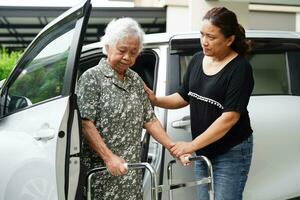 verzorger helpt aziatische bejaarde vrouw met een handicap om in haar auto te stappen, medisch concept. foto