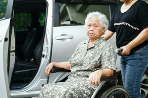 verzorger helpt aziatische bejaarde vrouw met een handicap om in haar auto te stappen, medisch concept. foto