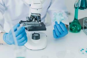 medisch of wetenschappelijk onderzoeker onderzoeken en experimenteren veelkleurig oplossing, flacon en microscoop in de laboratorium of in de laboratorium door vervelend blauw handschoenen en wit kleding volledig. foto