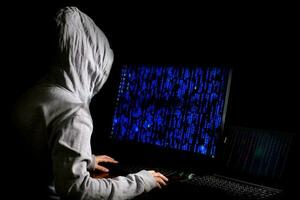 vrouwelijke hacker breekt in bij gegevensservers van de overheid en infecteert hun systeem met een virus op zijn schuilplaats, donkerblauwe atmosfeer, dame met kap die laptop met binaire codeachtergrond gebruikt, malwareconcept foto