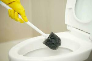 huisvrouwen gebruik een borstel naar schoon de badkamer naar verwijderen aarde en nemen zorg van sanitair waren. foto