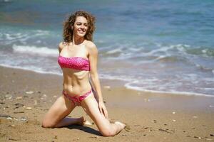 gelukkig vrouw in bikini zittend in de buurt zeewater foto