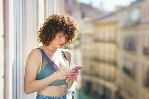 jong vrouw in beha en jeans met gekruld haar- terwijl browsen smartphone foto