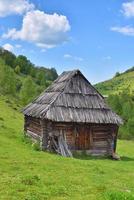eenzaam oud houten huis op een bergheuvel met groen gras tegen blauwe hemel