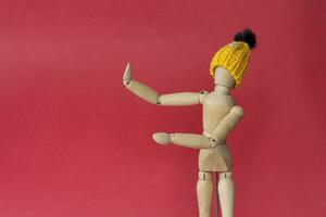een houten mannequin van een Mens in een gebreid geel hoed points naar een plaats De volgende naar hem. mannequin van een Mens gemaakt van hout Aan een rood achtergrond. foto