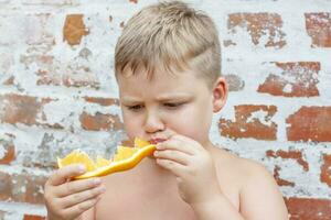 portret van kind. schattig jongen poseren en aan het eten een heerlijk oranje. de emoties van een kind. foto