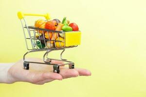 boodschappen doen kar met fruit en groenten Aan personen hand- Aan geel achtergrond. voedsel levering internet boodschappen doen concept foto