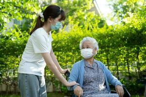 verzorger helpen en zorg Aziatisch senior vrouw geduldig vervelend masker zittend Aan rolstoel Bij verpleging ziekenhuis afdeling, gezond sterk medisch concept. foto