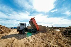 levering van zand naar de bouw plaats door vrachtauto met verheven lichaam foto