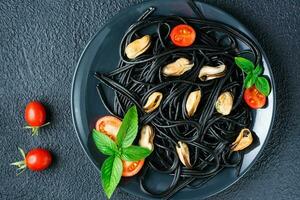 klaar om te eten zwart spaghetti met mosselen, tomaten en basilicum Aan een bord Aan een zwart achtergrond. voedsel fotografie in donker kleuren. top visie. detailopname foto