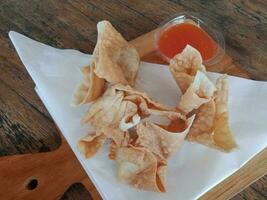 dichtbij omhoog visie van gebakken dimsum geserveerd met Chili saus Aan houten snijdend bord foto