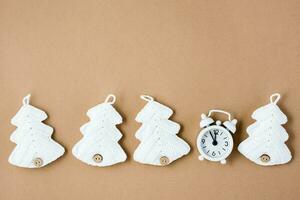 concept countdown Aan Kerstmis nacht. wit alarm klok Bij vijf naar twaalf en wit gebreid Kerstmis bomen Aan beige karton. top visie foto