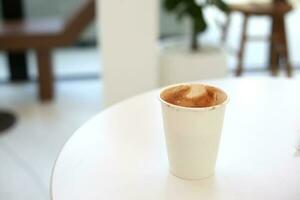 cacao melk papier kop Holding in vrouw hand- met wit tafel in cafe foto