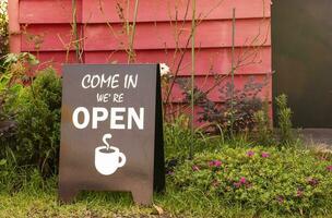 bruin teken met bericht komen in wij zijn Open en icoon koffie kop Aan glas Bij Ingang koffie winkel foto