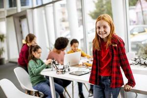 schattig klein meisje staan voor kinderen programmeren van elektrisch speelgoed en robots op robotica klas foto