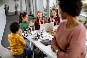 gelukkige kinderen met hun Afro-Amerikaanse vrouwelijke wetenschapsleraar met laptop die elektrisch speelgoed en robots programmeert bij robotica-klas foto