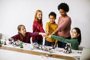 gelukkige kinderen met hun Afro-Amerikaanse vrouwelijke wetenschapsleraar programmeren elektrisch speelgoed en robots in robotica klas foto