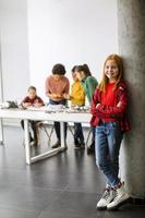 schattig klein meisje staan voor kinderen programmeren van elektrisch speelgoed en robots op robotica klas foto