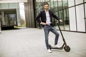 jonge zaken man in een casual kleding staande op elektrische scooter door een kantoorgebouw op een zakelijke bijeenkomst foto