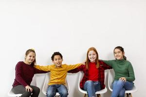 portret van schattige kleine kinderen in spijkerbroek zittend in stoelen tegen witte muur foto