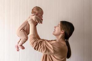 vrolijke mooie jonge vrouw met babymeisje in haar handen en haar met liefde thuis te kijken