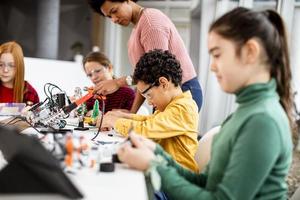 Afro-Amerikaanse vrouwelijke wetenschapsleraar met een groep kinderen die elektrisch speelgoed en robots programmeren bij robotica-klas