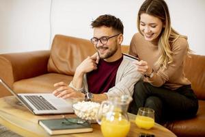 jonge vrouw en jonge man met behulp van laptop voor online betaling zittend op de bank thuis