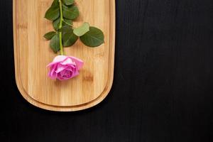 een roze roos ligt op een houten snijplank op een donkere achtergrond bovenaanzicht met ruimte voor tekst