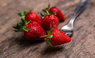 verse aardbeien en een bes op vork stilleven op donkere houten achtergrond foto