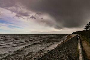 kust landschap met water golven, strand en dreigend donker bedreigend storm wolk in voorjaar foto