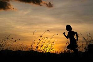 silhouet van kind meisje draait op de weide bij zonsondergang achtergrond. foto