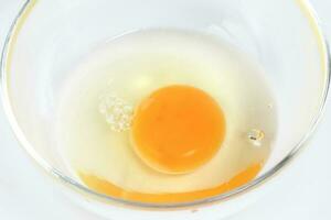 rauw ei dooier en wit vloeistof in transparant glas kom wit achtergrond foto