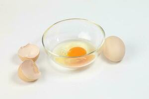 rauw ei dooier en wit vloeistof in transparant glas kom eierschaal wit achtergrond foto