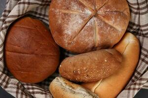 vers gebakken brood brood bun rollen ronde lang mengen waarheid verpakt in geruit keuken kleding stof servet handdoek over- zwart achtergrond foto