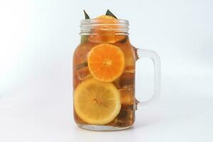 vloeistof ijs citroen oranje thee met plak groen blad kaneel stok in transparant glas pot mok Aan wit achtergrond foto