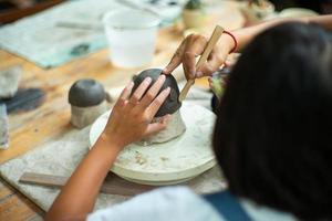 close-up hand van een leraar die de student onderwijst in het vormen van de klei met een houten gereedschap. foto